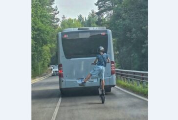 Момче с тротинетка изпреварва автобус по пътя, кара я на една гума